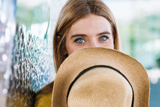 Young blonde woman with beautiful blue eyes covering face with straw hat