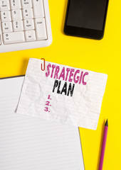Text sign showing Strategic Plan. Business photo text a systematic process of envisioning a desired future Crumpled white paper on table with paper clips clock mobile and pc keyboard