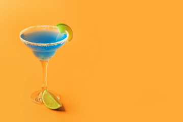 Blue margarita alcoholic cocktail with tequila, liqueur, lime juice, salt and ice, summer yellow background, copy space