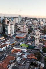 Fototapeta na wymiar Aerial view of streets and avenues in Pinheiros neighborhood with commercial buildings and small houses at dusk on sunny summer day. The neighborhood has old houses and modern office buildings.