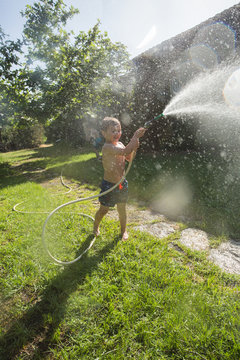 Little laughing kid in shorts and with bare feet splashing water from garden hose
