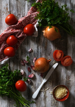 From above Fresh ripe tomatoes and onions with garlic and parsley placed on shabby wooden tabletop near napkin