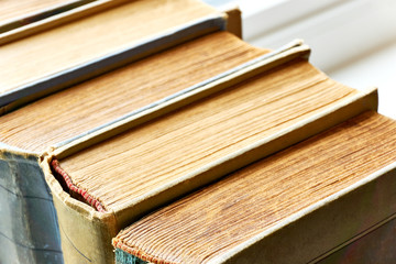 Old books in a row. Monochrome coloured weathered, aged, stained and torn antique books with red white headband. Closeup shot with selective focus.  