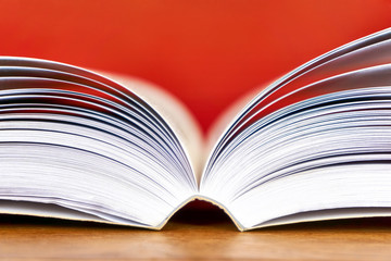 Open text book with visible pages on wooden desk against a red background. Back to school, education or study concept. Closeup side view shot with selective focus. and copy space