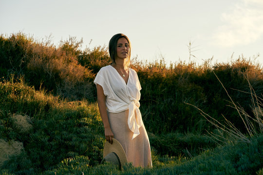 Young beautiful female model in white clothes smiling and looking at camera in nature