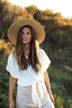 Young beautiful female model in white clothes smiling and looking at camera in nature