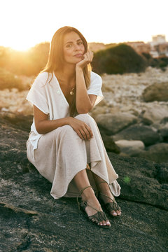 Beautiful young female model sitting and posing on rock looking at camera