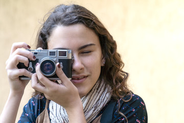 Young pretty girl taking picture with digital vintage camera in garden on sunny summer day with clear wall background. Travel, art, freedom, photography, youth and technology concept.
