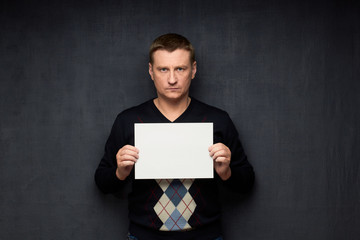 Portrait of serious man holding white blank paper sheet