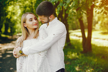 Fototapeta premium A beautiful and gentle girl with light hair and a white dress is walking in a sunny summer forest with her handsome guy in a white shirt and dark pants