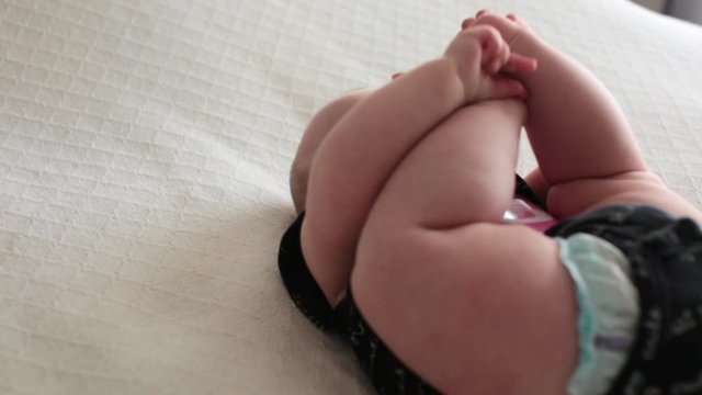   Cute Happy 5 month Baby Girl in Black Outfit with number 5 sticker, lying and playing on the Bed, played with legs and sucks big toe