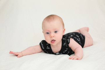 Fototapeta premium Cute Happy 5 month Baby Girl in Black Outfit with number 5 sticker, lying and playing on the Bed, played with legs and sucks big toe