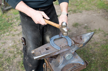 Blacksmith forges horseshoe with hammer on anvil. Ancient craft. Village craft. Blacksmith working...