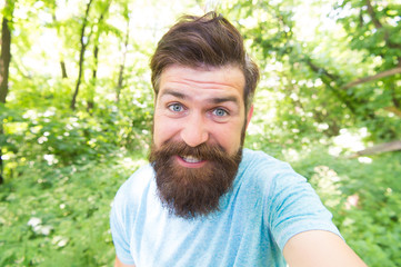 Naklejka na ściany i meble Beard can make a man look more brutal. Happy man with long mustache and beard hair outdoor. Brutal man smiling with unshaven face and stylish haircut. Bearded man in casual style on natural landscape