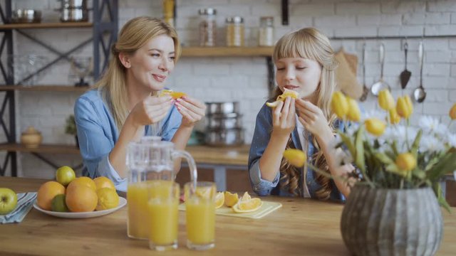 Mom and daughter eat oranges while sitting in the dining room. Juicy ripe orange and happy family concept. 4K