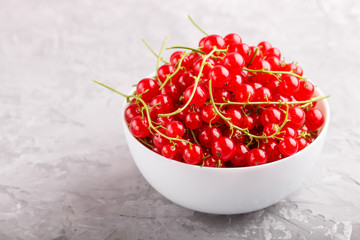 Fresh red currant in white bowl on gray concrete background. side view.