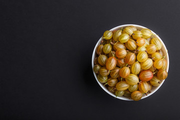 Fresh green gooseberry in white bowl on black background. top view.