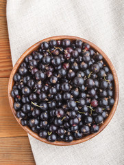 Fresh black currant in wooden bowl on wooden background. top view.