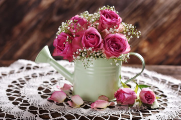 bunch of pink roses in a watering can on wooden table