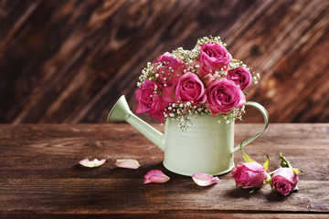 bunch of pink roses in a watering can on wooden table