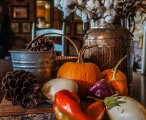 Autumn vegetable arrangement on a wooden table in a farmhouse keeping room, selective focus on foreground, including pumpkin purple bell peppers white eggplant orange and red