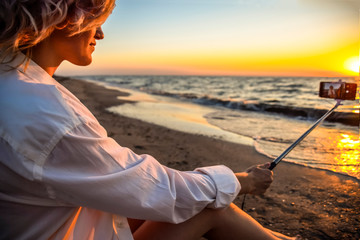 Selfie with selfie stick on the beach at sunset with a glass of champagne