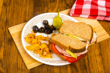 Ham and Cheese Sandwich on Wheat Bread with Chips and Olives on Rustic Table