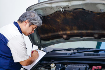 The car mechanic is recording the checklist of the car's bad condition.