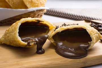 One open tradional Brazilian fried pastry called pastel stuffed with chocolate Brazilian dessert brigadeiro in a cutting board with half light