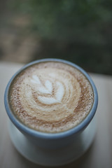 Hot cappuccino coffee cup with tree shape latte art milk foam on wood table near window in garden at cafe restaurant