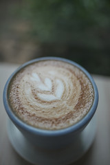 Hot cappuccino coffee cup with tree shape latte art milk foam on wood table near window in garden at cafe restaurant