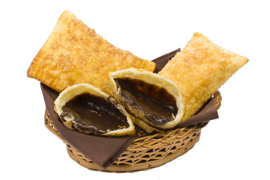 Tradional Brazilian fried pastry called pastel stuffed with chocolate Brazilian dessert brigadeiro with one open in a basket isolated in white background