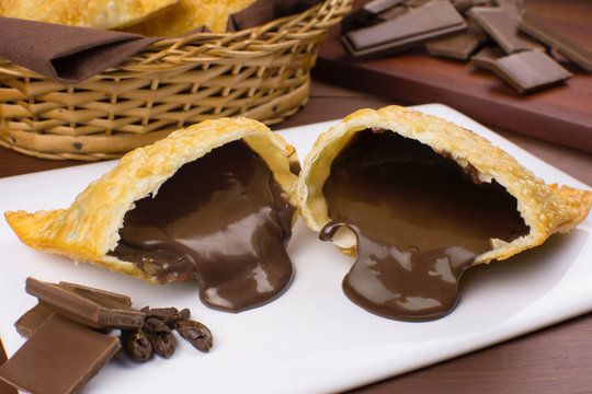 One open tradional Brazilian fried pastry called pastel stuffed with chocolate Brazilian dessert brigadeiro in plate in wood background