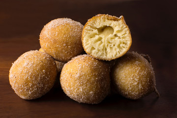 Traditional Brazilian mini fried cakes called bolinho de chuva with one open in wood background