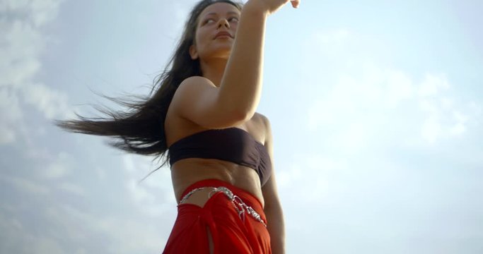 tempting woman is dancing movement of belly dance outdoors against sky