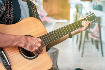 Young man enjoy playing an acoustic guitar in the coffee bar close up.