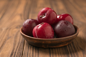 Large large ripe plums in a clay Cup on a wooden table.