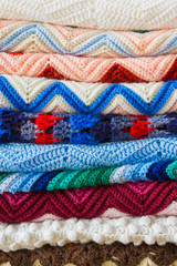 A colorful stack of folded crochet afghans; cozy, handmade crochet blankets in a pile