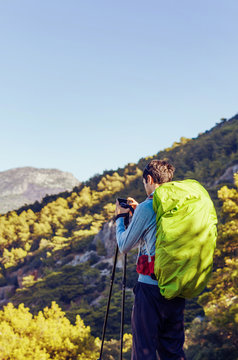 Man with trekking poles and backpack taking picture on a mountain trail