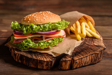 Tasty grilled homemade burger with beef, tomato, cheese, cucumber and lettuce. Delicious grilled burgers. Craft beef burger and french fries on wooden table. - obrazy, fototapety, plakaty