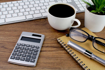 Office desk wooden table with computer,keyboard,calculator,pen,notebook,glasses and cup of coffee.Working desk table
