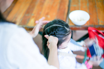 Top view hands of mother doing braid on her daughter hair in morning