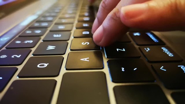 Close up shot of fingers typing on laptop keyboard and scrolling and clicking on trackpad.