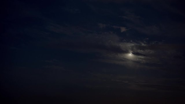 Night to day timelapse. Moon shines behind clouds as the blue sky appears during sunrise