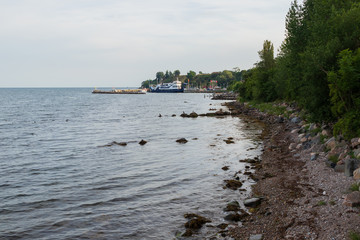 A stone beach on the island of Ven in southern Sweden with the ferry Stjernborg visible while stopping in the harbor of Bäckviken during a summer sunset. 