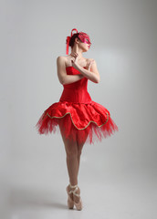 full length portrait of girl wearing red ballerina tutu and mask. dancing pose against a studio...