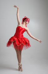 full length portrait of girl wearing red ballerina tutu and mask. dancing pose against a studio background.