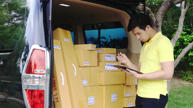 Young Asian Delivery man in yellow uniform checking list of package boxes on van before delivering to customer, Delivery Service