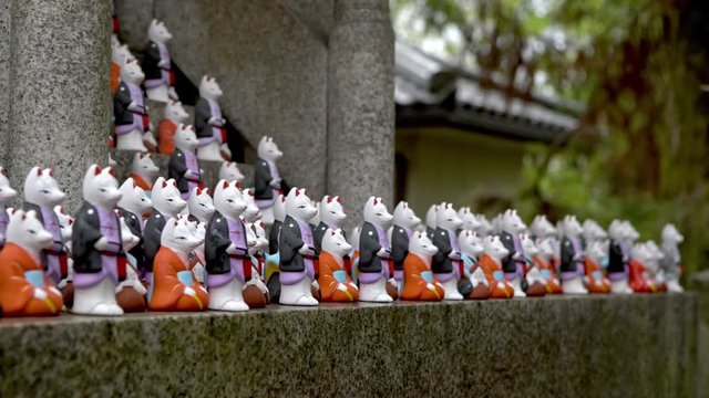 4K, Hundreds of small statues of lucky foxes in the famous Shinto shrine. Beautiful japanese amulets in a small temple of Fushimi Inari Taisha. The worship of Kitsune in a Japan sanctuary.-Dan