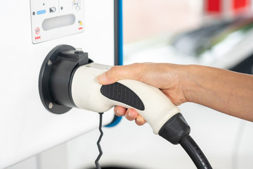 The driver female hand picks up a cable to charge the electric vehicle. Clean energy for vehicle.